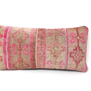 May include: Rectangular decorative pillow with a beige and pink patterned design. The pillow features a central section with a repeating floral pattern in pink, framed by vertical pink stripes. The overall texture appears woven.