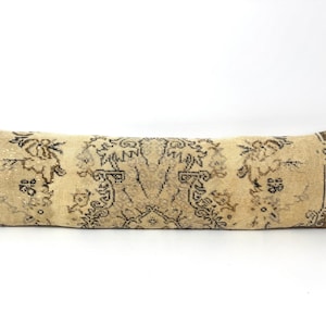 May include: A long, rectangular lumbar pillow featuring a vintage-style woven textile cover. The fabric displays a beige base color with intricate, symmetrical patterns in dark brown and muted charcoal gray, finished with brown end borders.