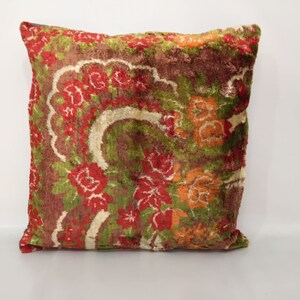 May include: A square pillow with a floral pattern in shades of red, orange, green, and brown. The fabric has a velvet-like texture.