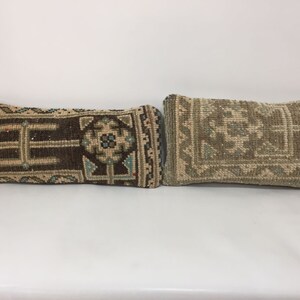 May include: Two rectangular decorative pillows with intricate geometric patterns. One pillow is primarily brown with beige, blue, and white accents. The other pillow is beige with a similar pattern in shades of green and beige. The pillows are side by side.