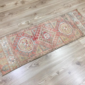 May include: A vintage Turkish runner rug with a geometric pattern in shades of red, beige, and blue. The rug has a faded, distressed look and is perfect for adding a touch of bohemian style to any room.