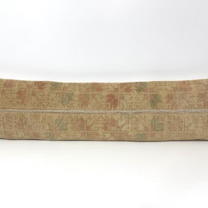 May include: A long, rectangular lumbar pillow featuring a woven textile cover in muted beige, tan, and brown tones. The fabric displays a faded, repeating floral pattern in soft shades of sage green and terracotta, with a horizontal seam across the center.
