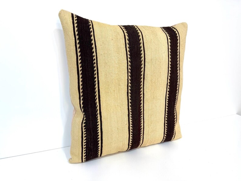 May include: A square throw cushion featuring a woven texture with a pattern of wide, dark brown vertical stripes alternating with wider beige sections. The dark brown stripes are bordered by thin, intricate, lighter-coloured zigzag lines.