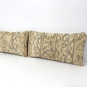 May include: Two rectangular throw pillows with a beige and brown patterned design. The pillows have a vintage, distressed look, with a repeating pattern of vertical stripes and floral motifs. The pillows are made of a woven fabric.