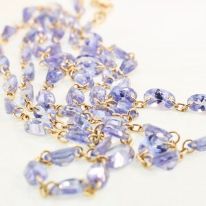 May include: A gold chain necklace with purple gemstone beads. The chain is made of small, linked metal pieces. The beads are oval-shaped and have a slightly irregular shape.