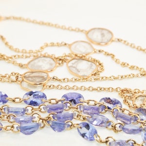 May include: A multi-strand necklace with a gold chain and alternating clear and purple gemstones.