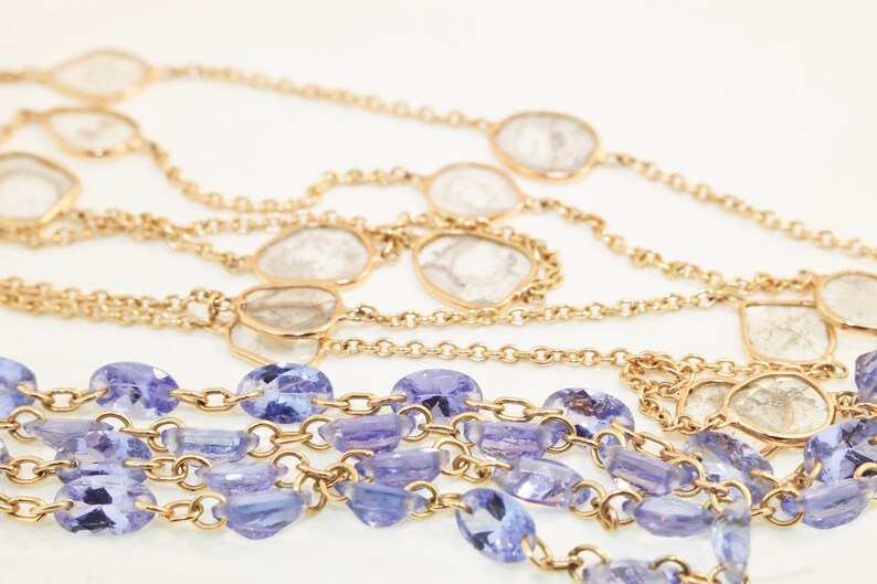 May include: A multi-strand necklace with a gold chain and alternating clear and purple gemstones.