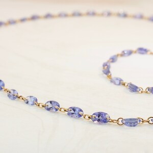 May include: A delicate gold chain necklace with oval-shaped amethyst gemstones. The necklace is laid out on a white surface.