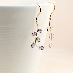 May include: A pair of gold dangle earrings with a delicate branch design and purple gemstones.