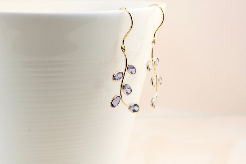 May include: A pair of gold dangle earrings with a delicate branch design and purple gemstones.