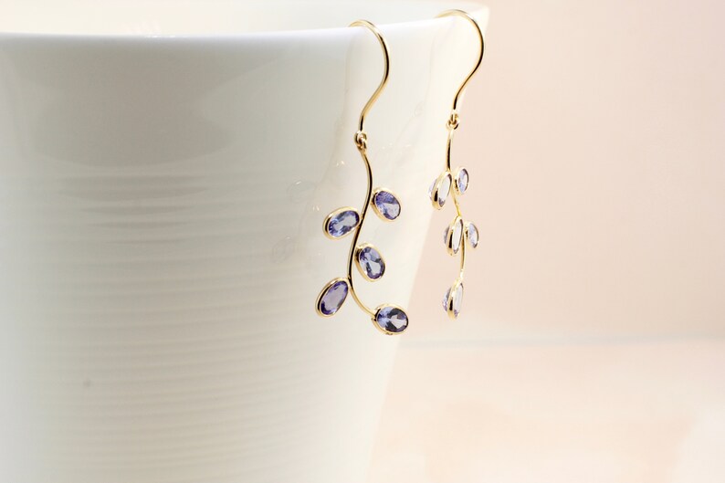 May include: A pair of gold dangle earrings with purple gemstones shaped like leaves.