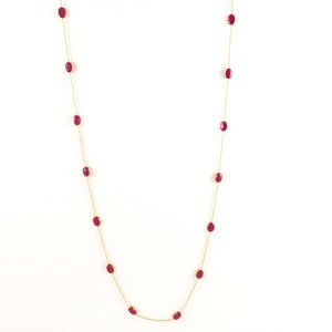 May include: A long gold chain necklace with oval-shaped red gemstones.