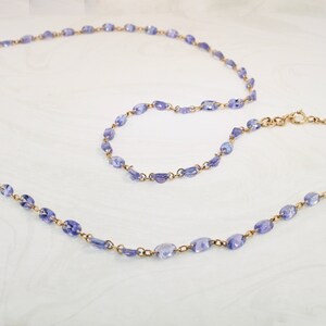 May include: A delicate gold chain necklace with a long and short strand, both adorned with small, oval-shaped amethyst gemstones.