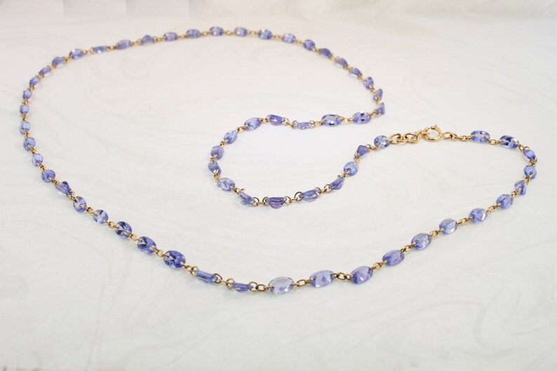 May include: A delicate gold chain necklace with a long and short strand, both adorned with small, oval-shaped amethyst gemstones.