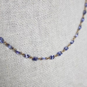 May include: A delicate gold chain necklace with small, oval-shaped blue gemstones.