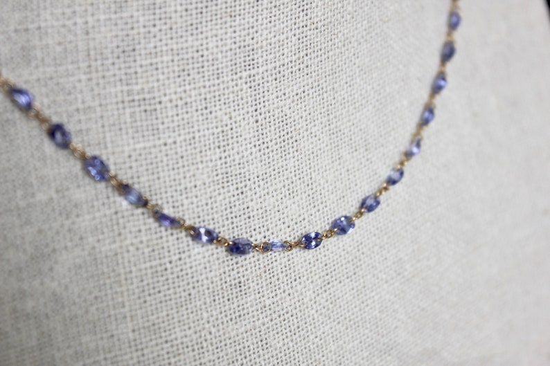 May include: A delicate gold chain necklace with small, oval-shaped blue gemstones.
