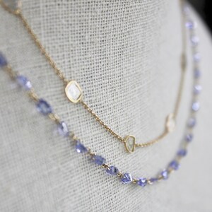 May include: Two gold necklaces with a delicate chain and small, clear gemstones. One necklace has a row of small, purple gemstones.