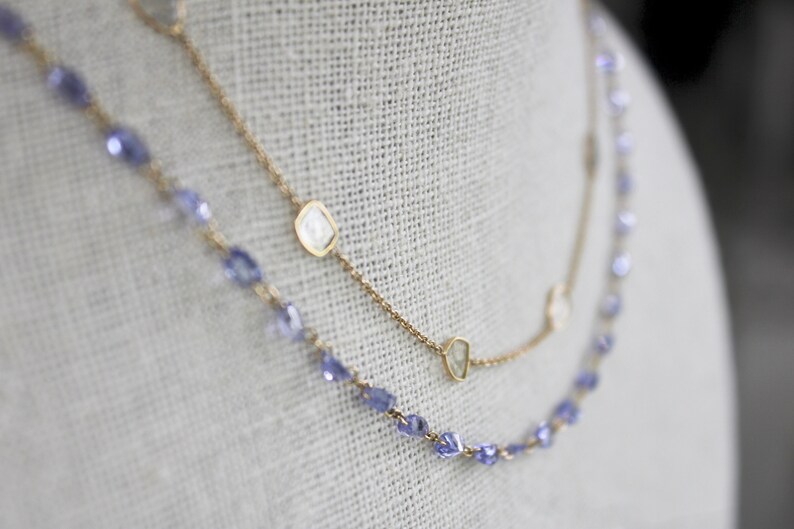 May include: Two gold necklaces with a delicate chain and small, clear gemstones. One necklace has a row of small, purple gemstones.