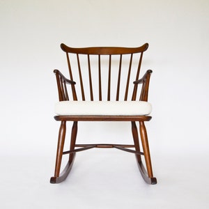 Peut inclure: Une chaise berçante en bois avec un coussin blanc. La chaise a un design simple et classique avec un dossier incurvé et une assise large.
