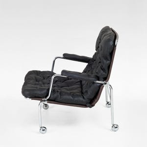 May include: Black leather armchair with a tufted seat and backrest. The chair has a dark brown frame and chrome arms and legs with rolling casters. The chair is set against a white background.