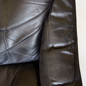 May include: Close-up of a section of a black leather sofa. The leather is stitched in a geometric pattern. The armrest is visible on the right side, with a seam running vertically. The background is white.