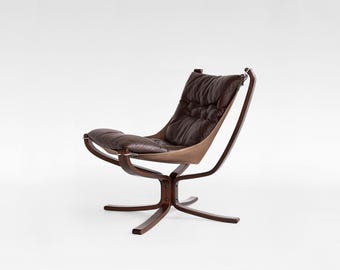 May include: A mid-century modern chair with a dark brown leather seat and backrest. The chair has a curved wooden frame and a star-shaped base. The seat appears to be approximately 30 inches wide.