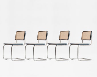 May include: Four chrome and cane dining chairs with black accents. The chairs are arranged in a row, facing the same direction.