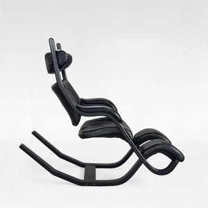 Puede incluir: Una mecedora negra con reposacabezas y reposabrazos curvos. La silla tiene un diseño elegante y moderno con una estructura negra y un asiento acolchado. Las dimensiones de la silla son de aproximadamente 102 cm de largo, 64 cm de ancho y 102 cm de alto.