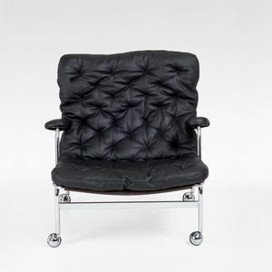 May include: Black leather armchair with a tufted back and seat. The chair has chrome arms and a chrome base with four small wheels. The chair is designed for comfort and style, suitable for a living room or office space.