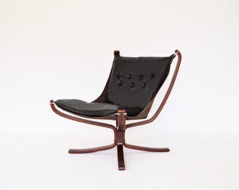 May include: A black leather chair with a wooden frame. The chair has a unique design with a curved back and a wide base.