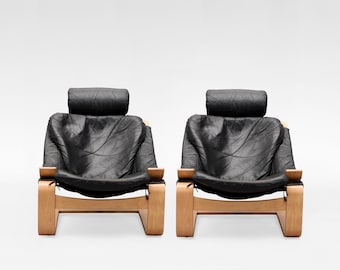 May include: Two matching armchairs with black leather upholstery and headrests. The chairs have a light wood frame and armrests. The design is modern and minimalist, suitable for a living room or lounge area.