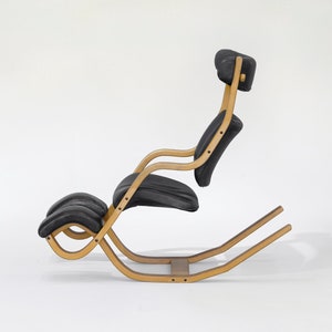 Puede incluir: Una silla mecedora de cuero negro con un marco de madera. La silla tiene un reposacabezas y un reposapiés.