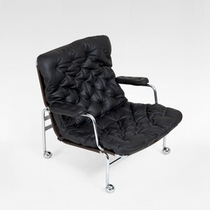 May include: Black leather armchair with a tufted back and seat. The chair has a chrome frame and armrests. The chair sits on four small chrome wheels. The chair is a modern design.