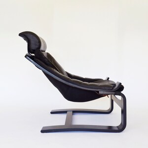 May include: A black leather and wood lounge chair with a headrest. The chair has a curved wooden frame and a cushioned seat. The chair is designed for relaxation and comfort.