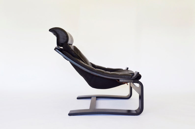 May include: A black leather and wood lounge chair with a headrest. The chair has a curved wooden frame and a cushioned seat. The chair is designed for relaxation and comfort.