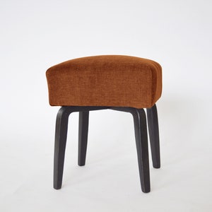May include: A brown upholstered stool with four black wooden legs.