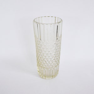 Può includere: Un vaso di vetro trasparente con un motivo a diamante e linee verticali. Il vaso è vuoto e ha una forma cilindrica.