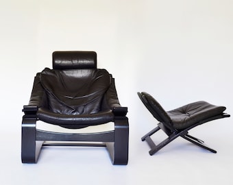 May include: Two black leather chairs. One is a large armchair with a headrest and wooden frame. The other is a smaller, folding chair with a similar design. Both chairs have a modern, mid-century aesthetic.
