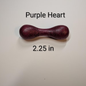 May include: A wooden, hourglass-shaped object with a deep purple hue. The text "Purple Heart" and "2.25 in" are displayed. The wood grain is visible, adding texture to the piece.