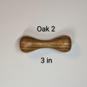 May include: A wooden dumbbell-shaped object made of oak, with the text "Oak 2" and "3 in" printed on the image. The object is approximately 3 inches long.