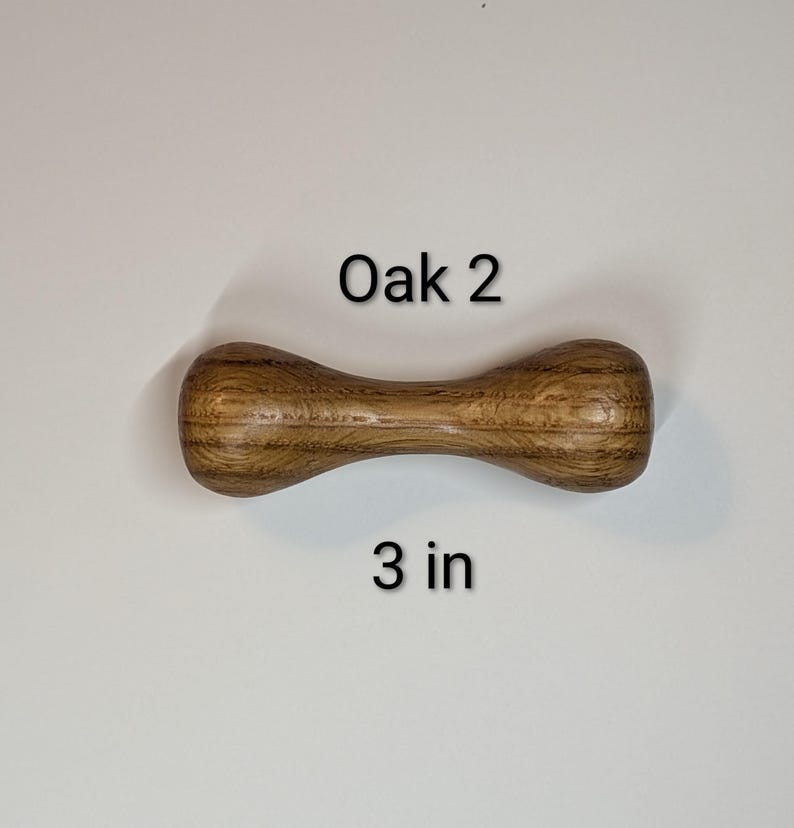 May include: A wooden dumbbell-shaped object made of oak, with the text "Oak 2" and "3 in" printed on the image. The object is approximately 3 inches long.