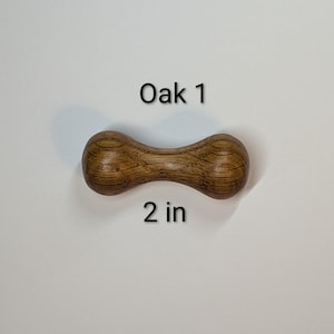 May include: A wooden dumbbell-shaped object made of oak. The object is brown with visible wood grain and the text "Oak 1" and "2 in" are printed on the image.
