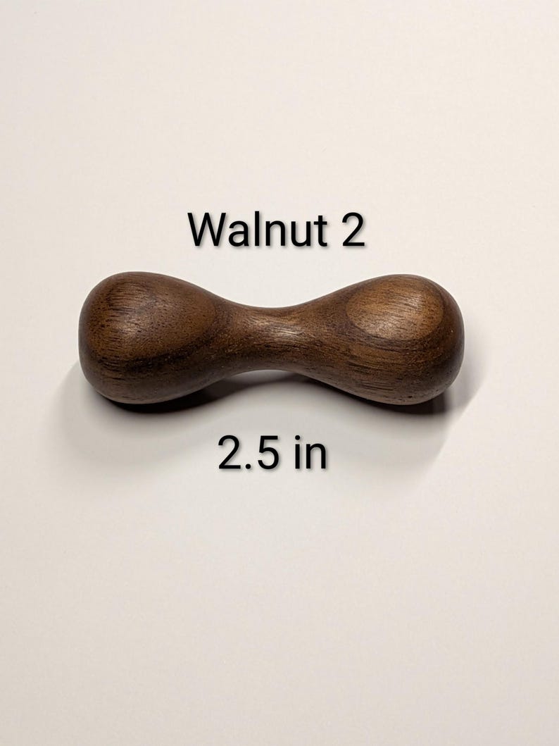May include: A dark brown, wooden dumbbell-shaped object. The text "Walnut 2" is above the object, and "2.5 in" is below it. The object is approximately 2.5 inches long.