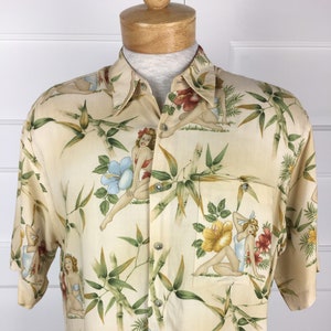 Puede incluir: Camisa crema con botones con un estampado tropical con tallos de bambú, flores y figuras estilo pin-up. La camisa de manga corta tiene un cuello clásico y un bolsillo en el pecho.