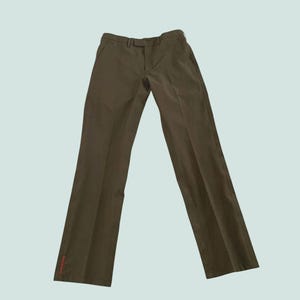 Pode incluir: Calças verde-oliva com design de perna reta. As calças têm fecho de botão e zíper, presilhas para cinto e um pequeno detalhe vermelho perto da bainha. As calças são feitas de tecido liso.