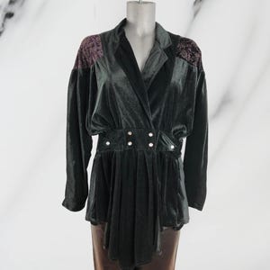 May include: A dark green velvet blazer with a wrap-style front and a cinched waist. The blazer has a high collar and long sleeves. The fabric has a subtle sheen and the blazer features a decorative silver buckle at the waist.