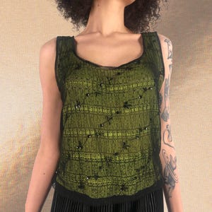 Puede incluir: Un top verde sin mangas con lentejuelas negras y una tela transparente. El top tiene un escote redondo y una silueta ajustada.
