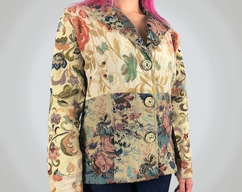 Puede incluir: Una chaqueta de manga larga con un patrón floral de tapiz multicolor en tonos crema, verde, rosa y azul. La prenda presenta una solapa con muesca, tres botones redondos decorativos en la parte delantera y un corte estructurado.