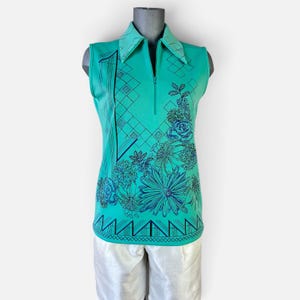 May include: A sleeveless turquoise polo shirt featuring a quarter-zip neckline and a pointed collar. The shirt is decorated with a dark blue graphic print consisting of a geometric diamond pattern, floral motifs, and a triangular border at the hem.