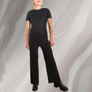 Puede incluir: Un mono negro con una parte superior de manga corta con un diseño brillante y texturizado. El mono tiene una silueta de pierna ancha y está hecho de una tela suave y elástica.